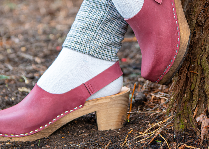 Person, viewing from the ankles down, wearing pink clogs leaning up against a tree